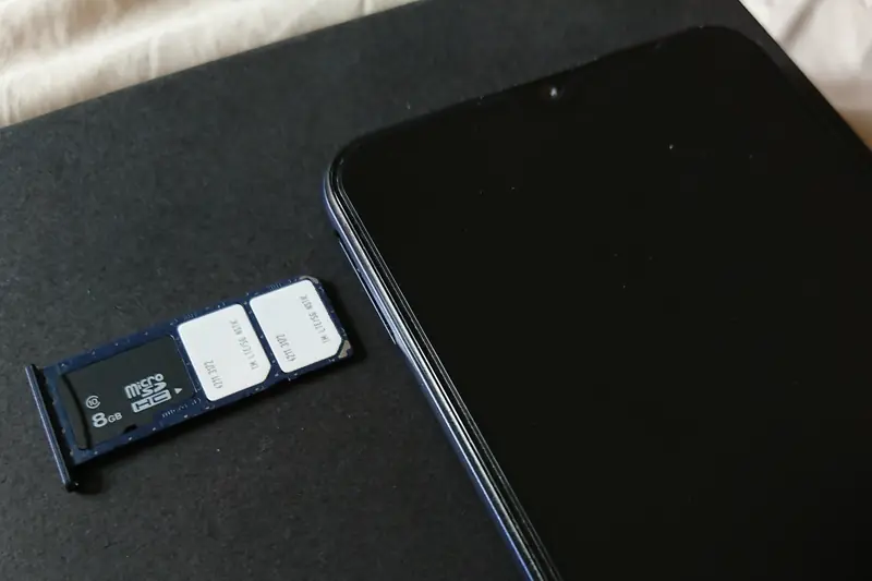 An ejected SIM tray holding two nano-SIM cards and a microSD card, lying next to a smartphone