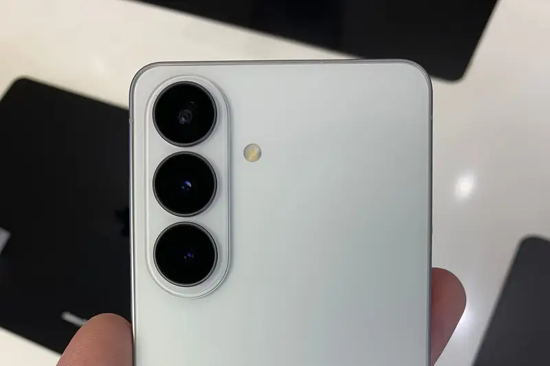 Back of a white Samsung Galaxy S26 held in a hand in a store, showing its three rear cameras
