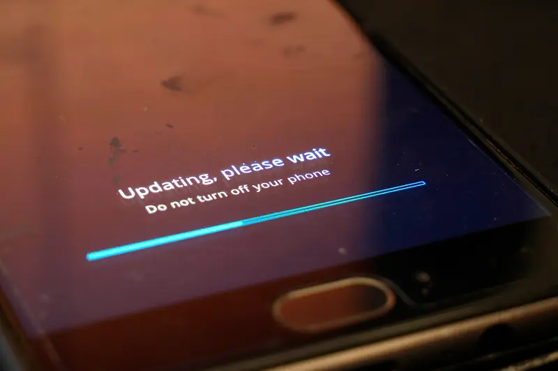 Close-up of an Android phone screen reading "Updating, please wait. Do not turn off your phone" above a progress bar