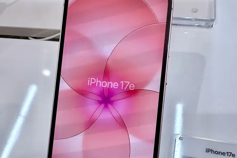 Pink iPhone 17e on a store display stand, its screen reading "iPhone 17e", with a Japanese price card beside it