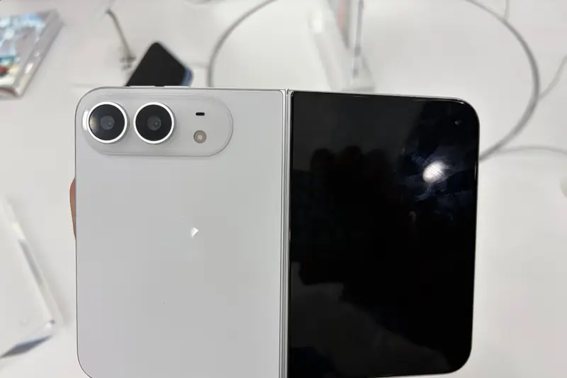 A white iPhone Duo held in a hand in a store, folded flat with a dual-camera module on the left half and a dark screen on the right
