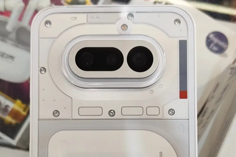 Back of a white Nothing Phone (4a) with a transparent design, showing its triple-camera module, among accessories in a shop