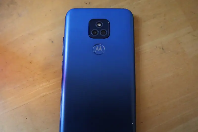 The back of a blue Motorola moto g play (2021) lying on a wooden desk