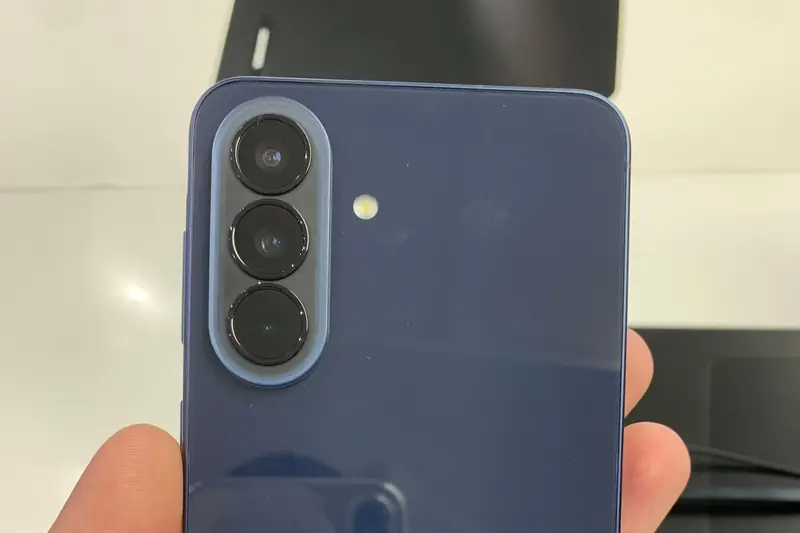 Back of a navy Samsung Galaxy A57 5G held in a hand in a store, showing its triple camera